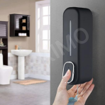 A black wall-mounted soap dispenser in a bathroom, with a hand pressing the button to dispense soap.