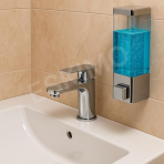A chrome soap dispenser mounted on a tiled wall above a white sink and chrome faucet.